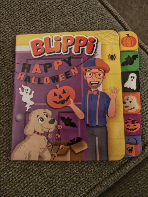 Picture of the book Blippi Happy Halloween.  Blippi stands in front of his door with his puppy with Halloween decorations. 